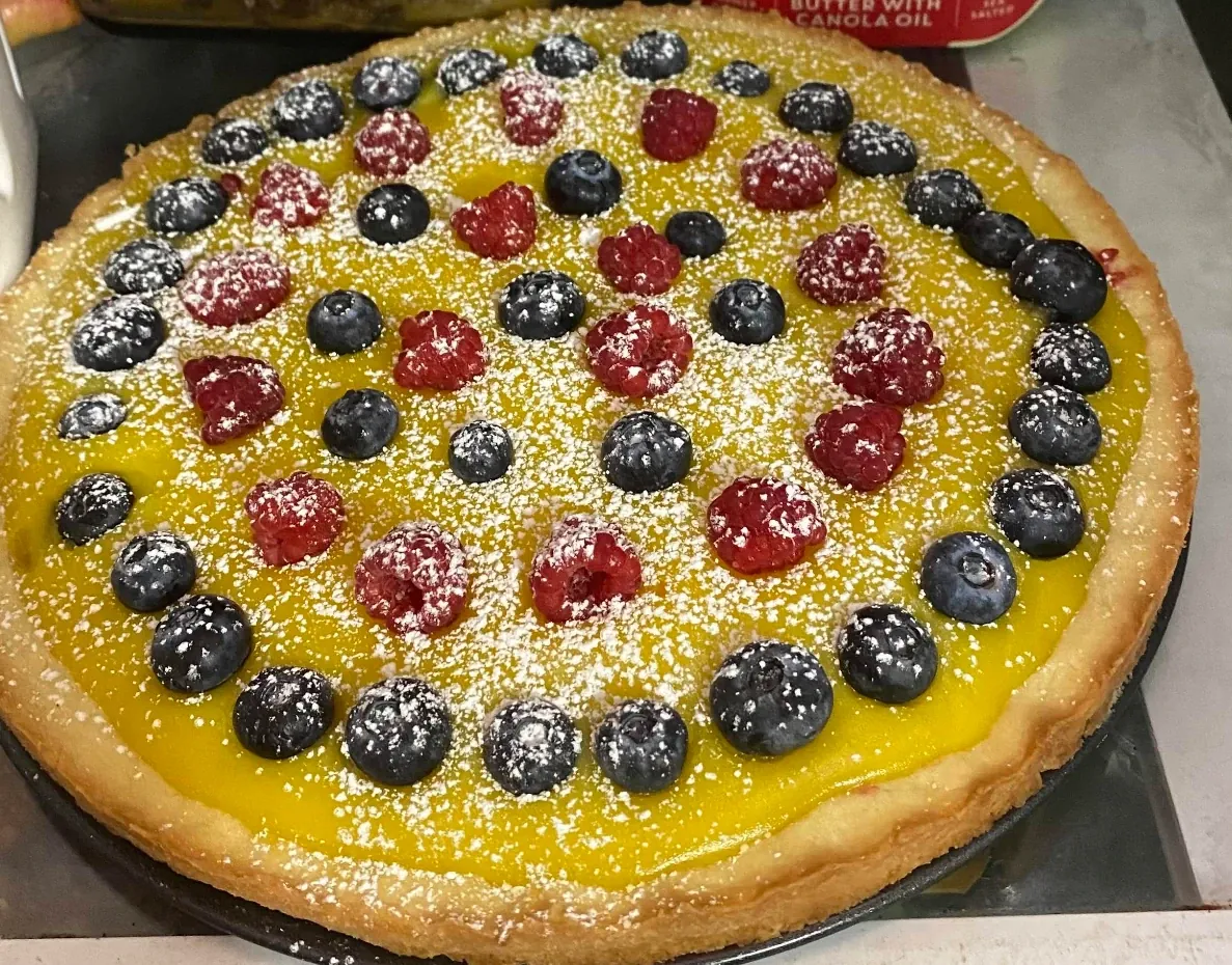A lemon fruit tart topped with blueberries, raspberries and powdered sugar